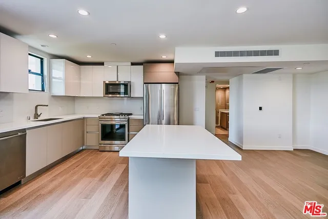 a large kitchen with kitchen island a sink dishwasher a refrigerator and a stove with wooden floor