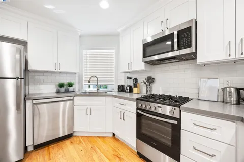 a kitchen with stainless steel appliances granite countertop white cabinets a sink a stove a refrigerator and microwave with wooden floor