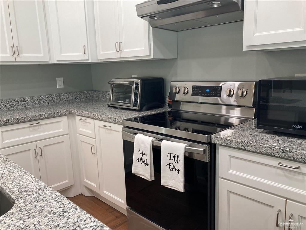 2103 South 6th Street McAllen, TX 78503 - Photo 6 of 33 Kitchen featuring stainless steel electric range oven, white cabinetry, exhaust hood, light stone countertops, and dark wood-style floors