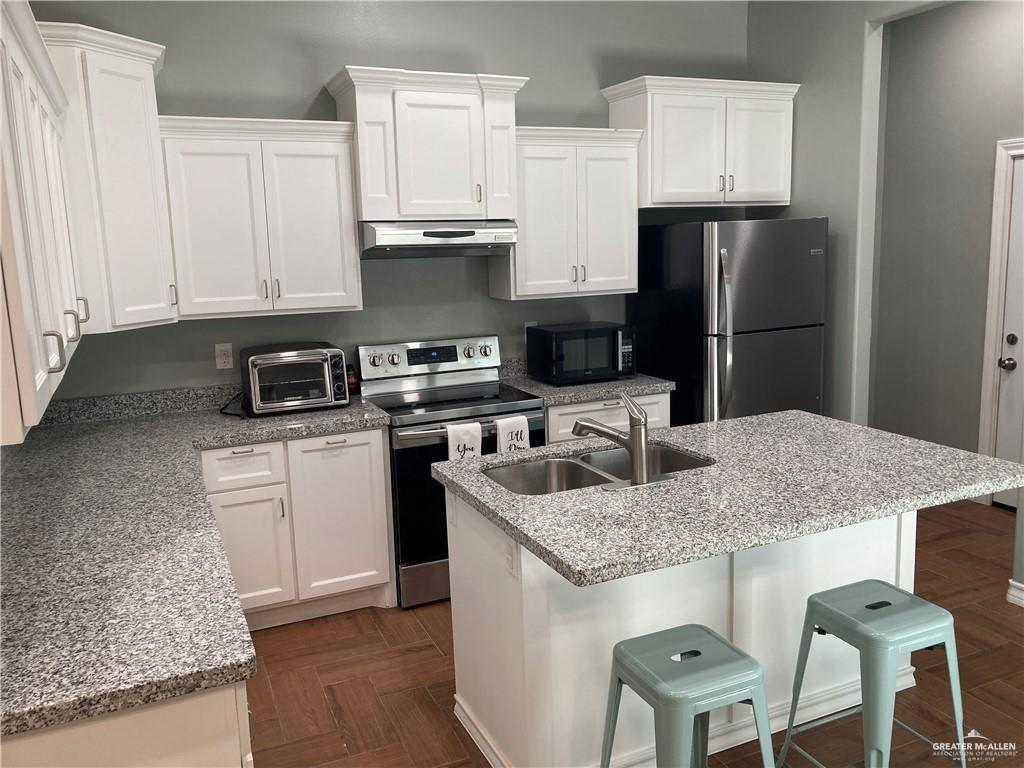 2103 South 6th Street McAllen, TX 78503 - Photo 7 of 33 Kitchen featuring white cabinetry, stainless steel appliances, a kitchen island with sink, light stone countertops, and a kitchen breakfast bar