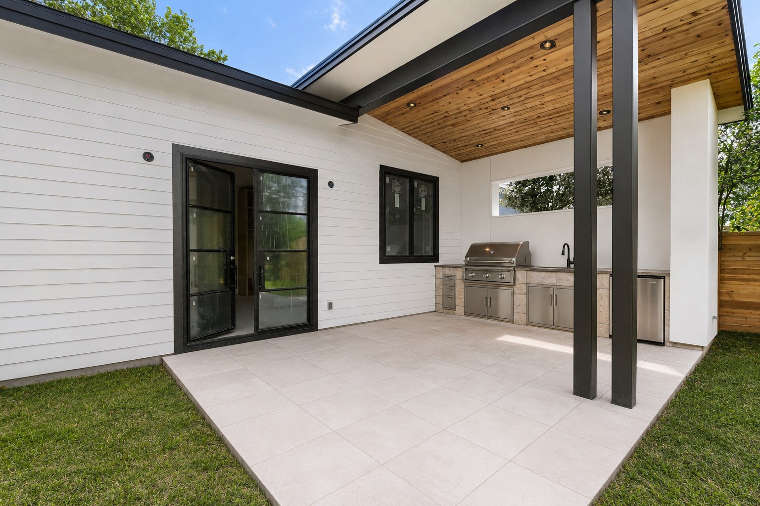 4603 Bucks Run Austin, TX 78744 - Photo 13 of 14 Outdoor living space featuring a tiled patio, full outdoor kitchen with built-in grill and sink, wood-paneled ceiling, and black-framed glass doors