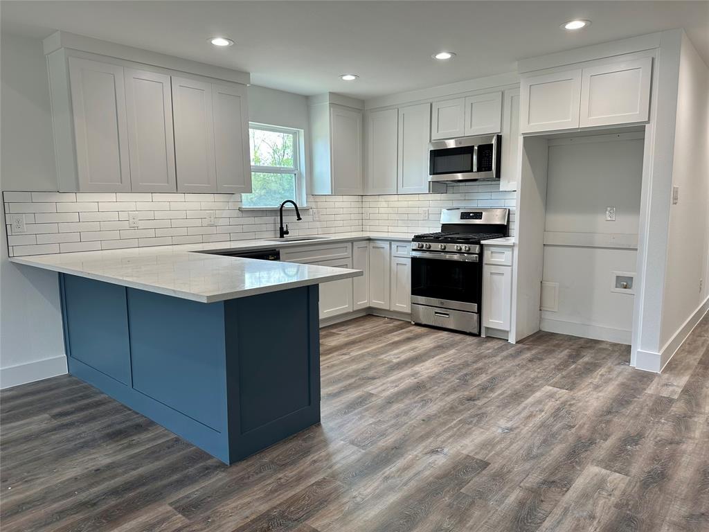 803 Sam Houston Street Rockwall, TX 75087 - Photo 5 of 10 Kitchen featuring white cabinets, appliances with stainless steel finishes, a peninsula, dark wood-style flooring, and light stone countertops