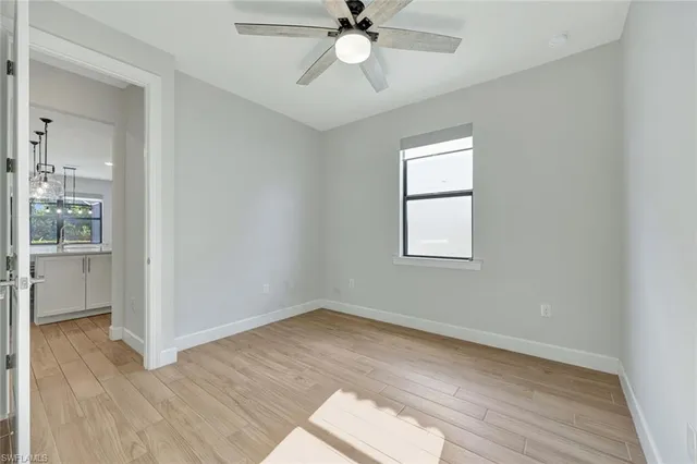 an empty room with wooden floor chandelier fan and windows