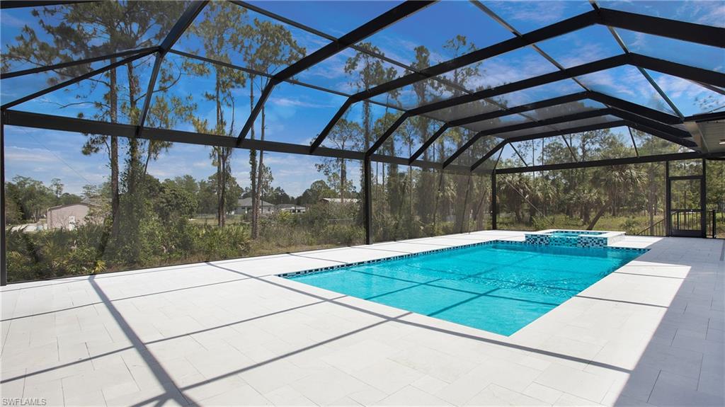 2343 Oil Well Road Naples, FL 34120 - Photo 27 of 46 Expansive screened enclosure featuring a rectangular pool with an integrated spa, set against a backdrop of mature trees and open skies