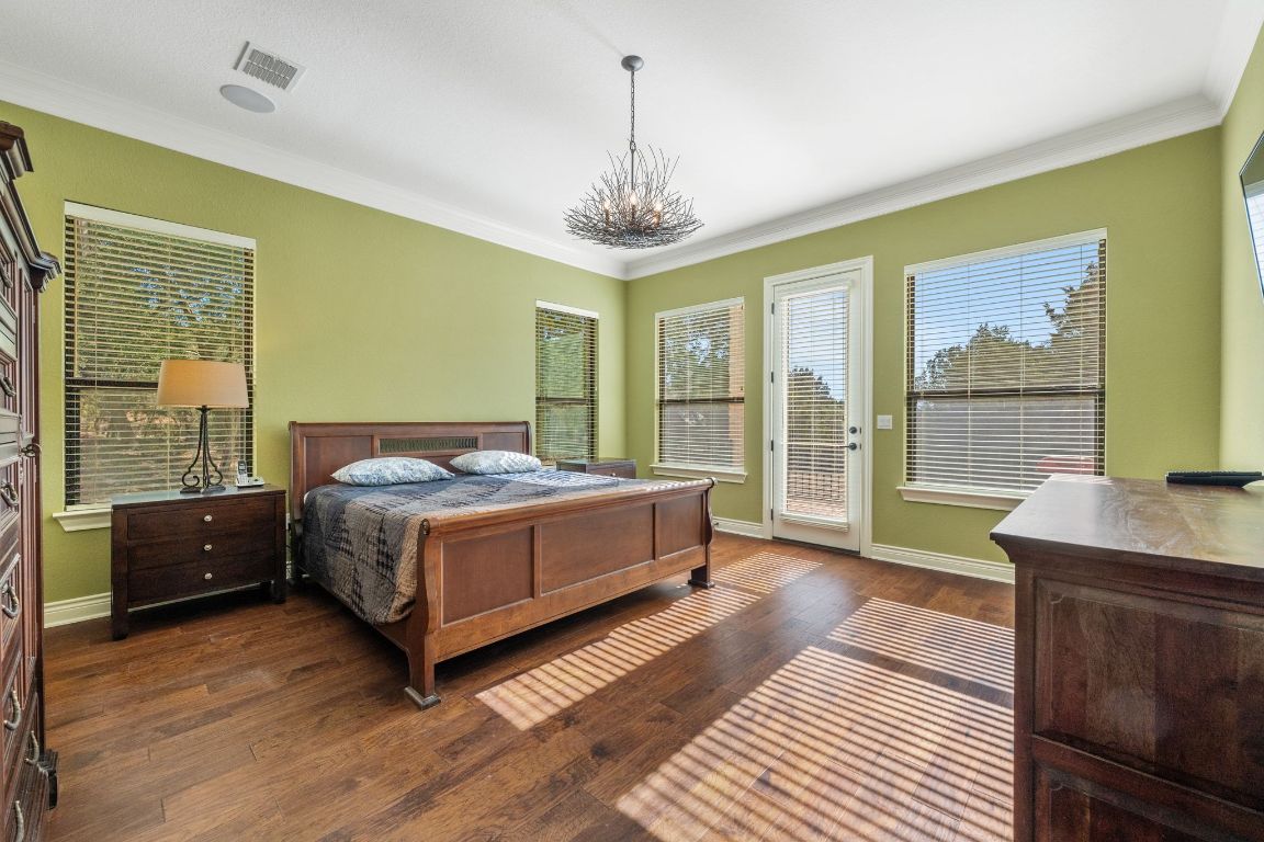 20607 Thurman Bend Road Spicewood, TX 78669 - Photo 12 of 40 Bedroom with a chandelier, dark wood-style floors, ornamental molding, access to outside, and multiple windows