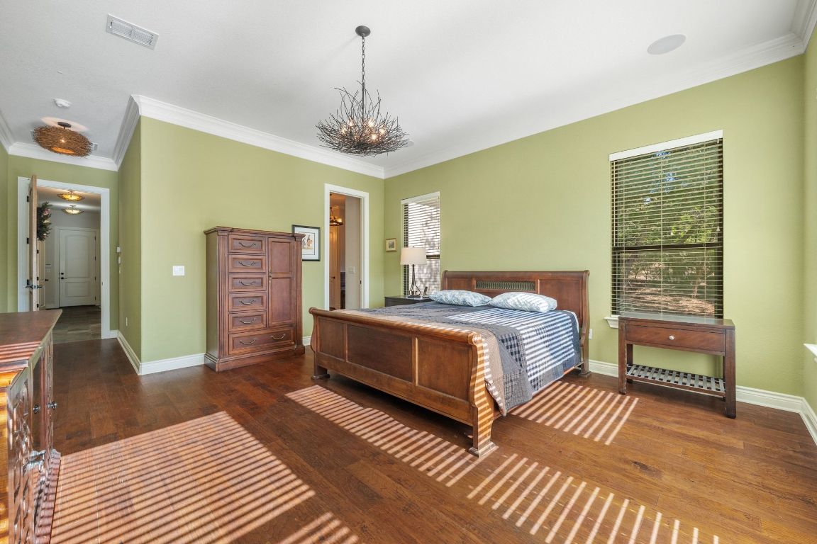 20607 Thurman Bend Road Spicewood, TX 78669 - Photo 13 of 40 Bedroom featuring dark wood-style flooring, ornamental molding, and a chandelier