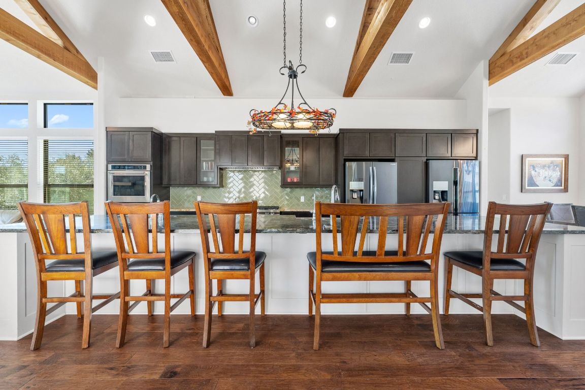 20607 Thurman Bend Road Spicewood, TX 78669 - Photo 6 of 40 Kitchen with recessed lighting, a breakfast bar area, decorative backsplash, glass insert cabinets, and hanging light fixtures