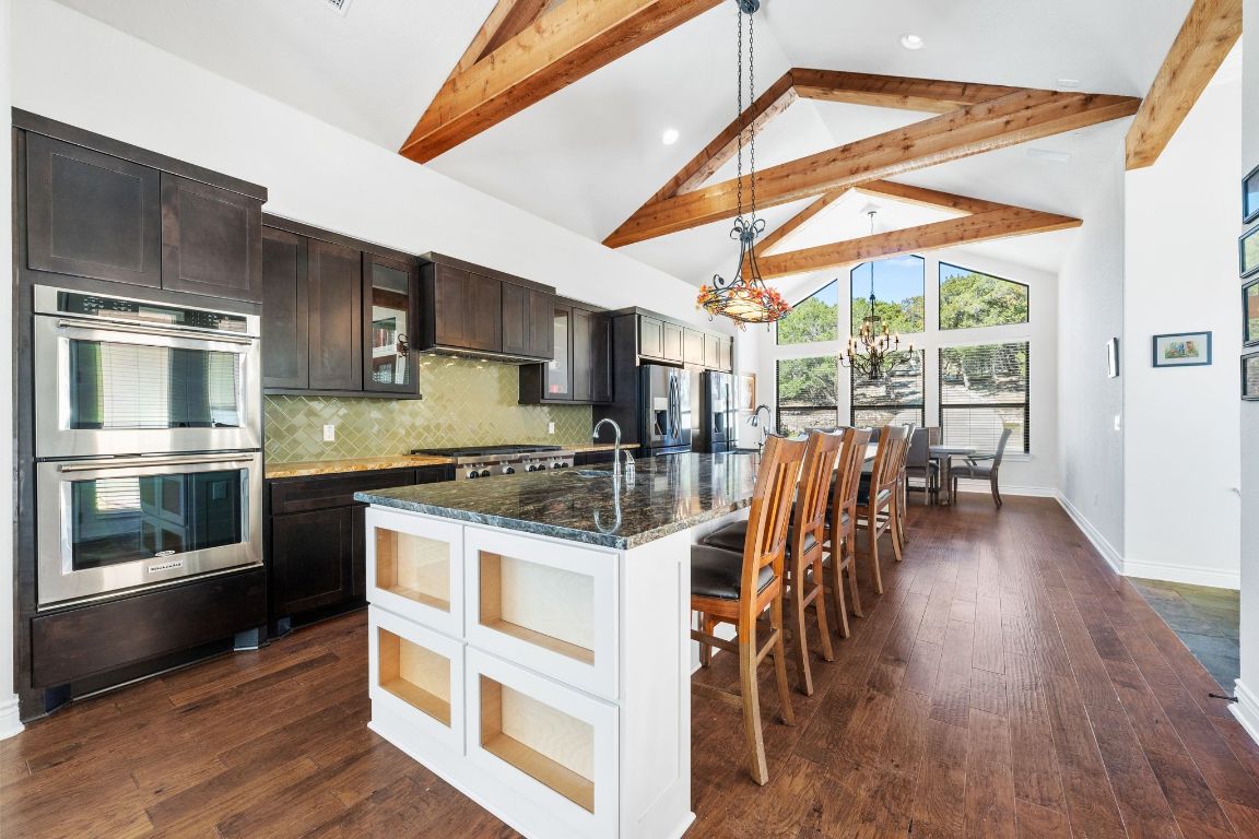 20607 Thurman Bend Road Spicewood, TX 78669 - Photo 7 of 40 Kitchen featuring high vaulted ceiling, a breakfast bar area, hanging light fixtures, double oven, and glass insert cabinets