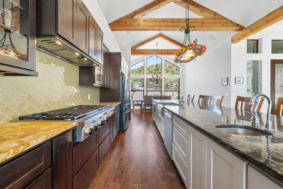 20607 Thurman Bend Road Spicewood, TX 78669 - Photo 8 of 40 Kitchen featuring dark stone countertops, dark brown cabinetry, backsplash, decorative light fixtures, and stainless steel appliances
