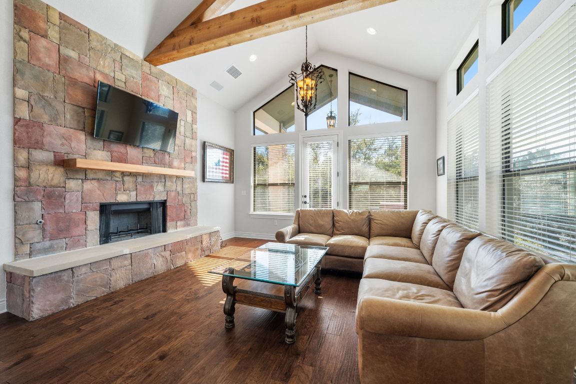 20607 Thurman Bend Road Spicewood, TX 78669 - Photo 9 of 40 Living room featuring a stone fireplace, a chandelier, high vaulted ceiling, dark wood-style floors, and beam ceiling