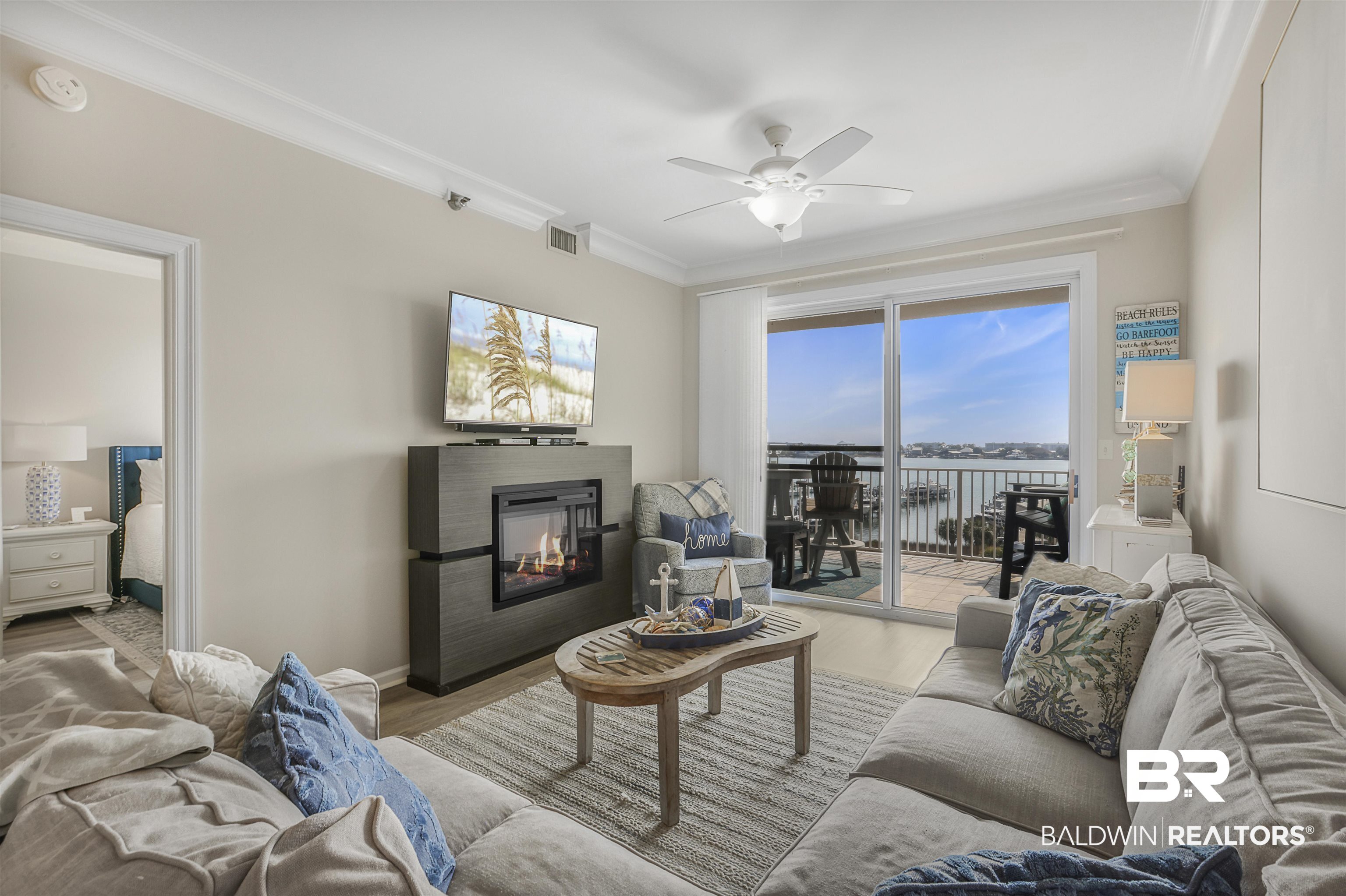 27282 Canal Road, Unit 511 Orange Beach, AL 36561 - Photo 8 of 29 Living room featuring a glass covered fireplace, crown molding, ceiling fan, and wood finished floors