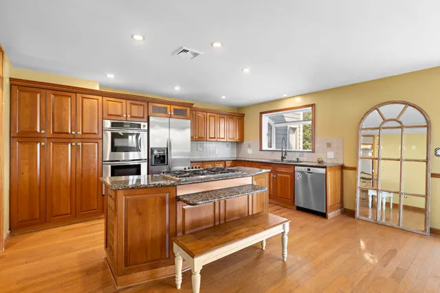 a kitchen with stainless steel appliances granite countertop a stove a sink dishwasher a refrigerator and wooden cabinets with wooden floor