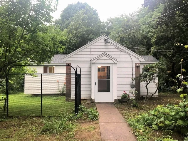 a view of a white house next to a yard with plants and large trees