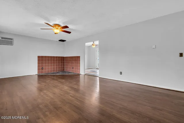 a view of an empty room with wooden floor and a ceiling fan