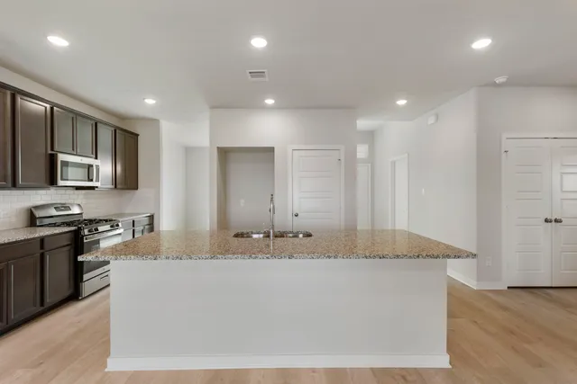 a large white kitchen with kitchen island granite countertop a stove a sink a refrigerator and white cabinets with wooden floor