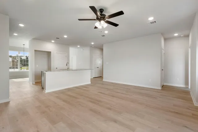a view of an empty room and kitchen with ceiling fan wooden floor and a ceiling fan