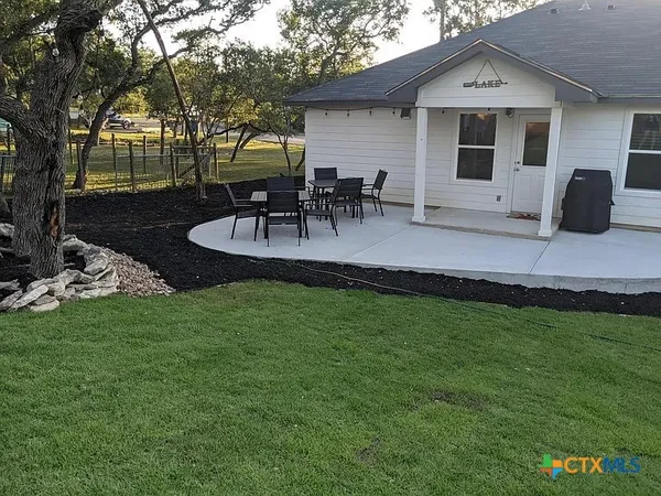 a view of a backyard with table and chairs potted plants and large tree