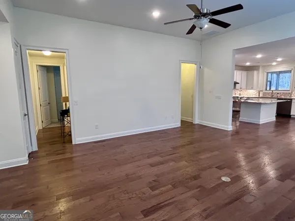 an empty room with wooden floor a ceiling fan and kitchen view