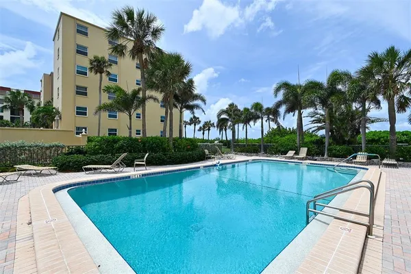 a view of a swimming pool with a lawn chairs under palm trees