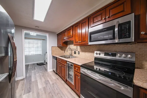 a kitchen with stainless steel appliances granite countertop wooden cabinets a refrigerator a sink and wooden floors