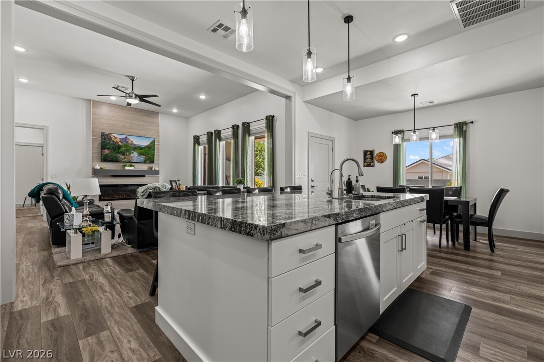 3020 Hannig Street Logandale, NV 89021 - Photo 13 of 75 A contemporary kitchen island features granite counters and stainless steel appliances, seamlessly connecting to a cozy living space with modern flooring.