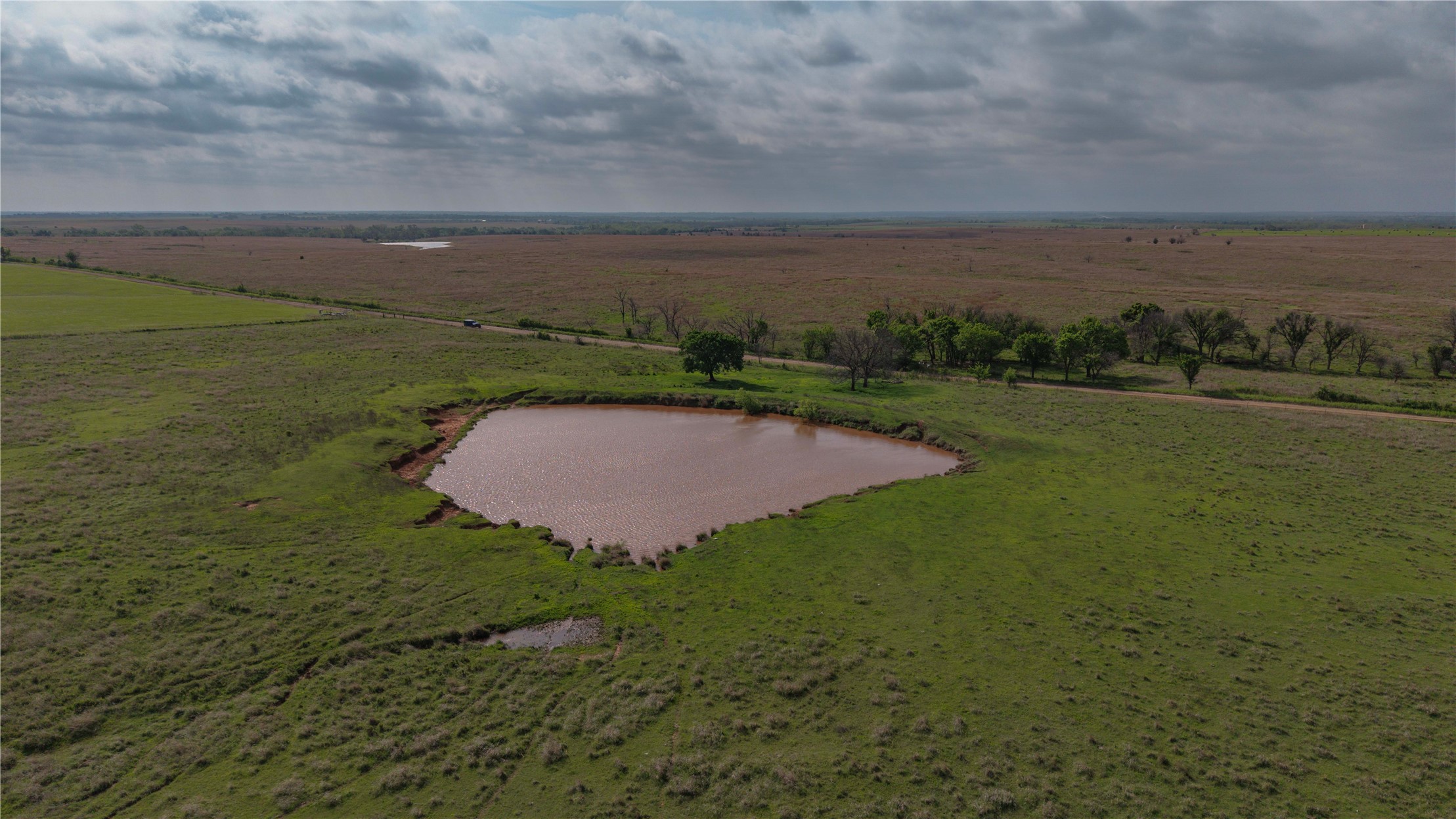42 East 4500 Road Morrison, OK 73061 - Photo 27 of 37 Expansive rural property featuring sprawling pastureland with lush green fields, a natural water retention pond, and mature tree clusters dotting the landscape