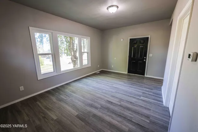 a view of an empty room with wooden floor and a window