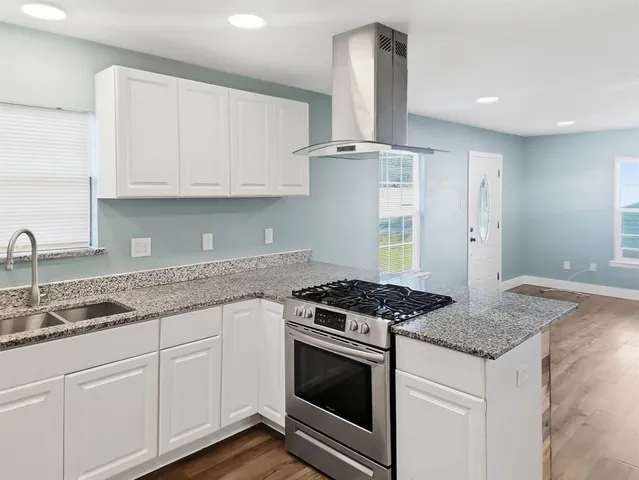 a large kitchen with granite countertop a stove top oven a sink and white cabinets with wooden floor