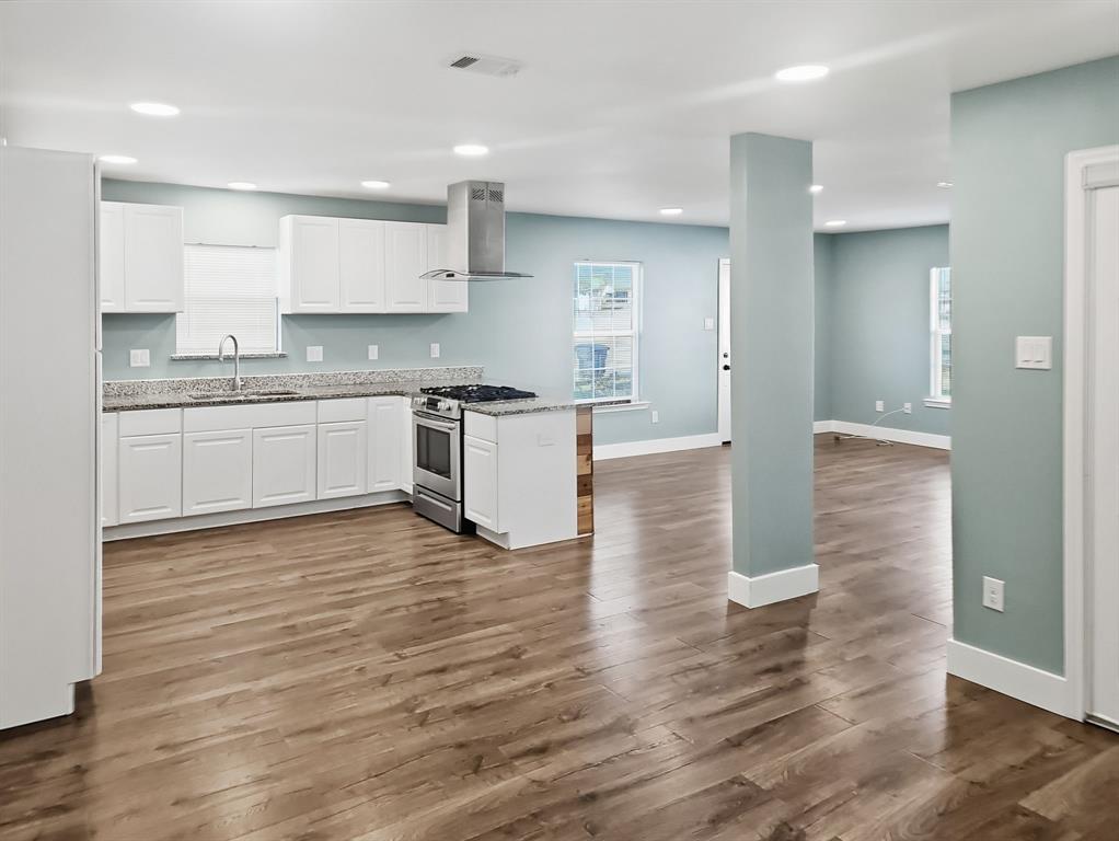 110 Ramsey Street Cleburne, TX 76031 - Photo 8 of 27 a large kitchen with granite countertop a stove top oven a sink and white cabinets with wooden floor