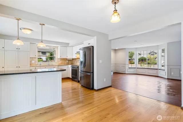 a kitchen with stainless steel appliances kitchen island granite countertop a refrigerator a stove a sink dishwasher and white cabinets with wooden floor