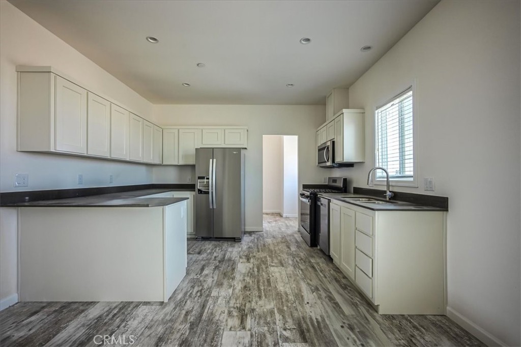 12076 Lager Road Phelan, CA 92371 - Photo 8 of 30 a kitchen with granite countertop a refrigerator oven a sink dishwasher and white cabinets with wooden floor
