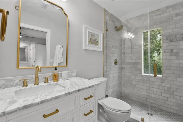 a bathroom with a granite countertop sink a toilet a mirror and shower