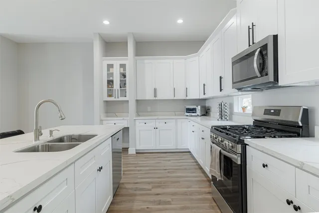 a kitchen with stainless steel appliances granite countertop a sink dishwasher stove and white cabinets with wooden floor