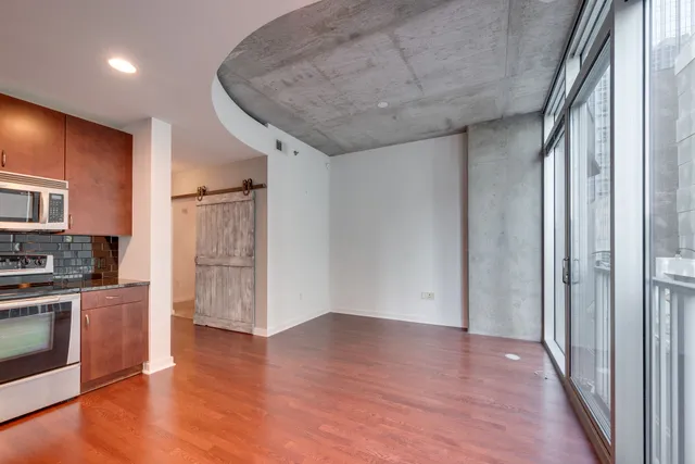 an empty room with wooden floor and a kitchen