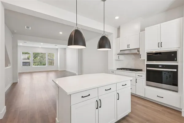 a kitchen with stainless steel appliances a stove a sink a wooden floor and white cabinets