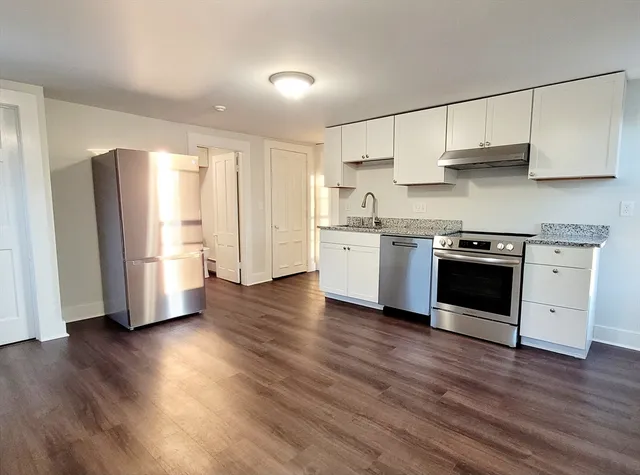 a kitchen with stainless steel appliances granite countertop a refrigerator a sink dishwasher a stove and white cabinets with wooden floor