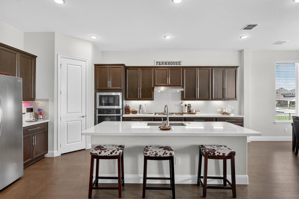 1420 Wolf Ridge Run Gunter, TX 75058 - Photo 27 of 40 a kitchen with stainless steel appliances kitchen island granite countertop a table chairs refrigerator and microwave