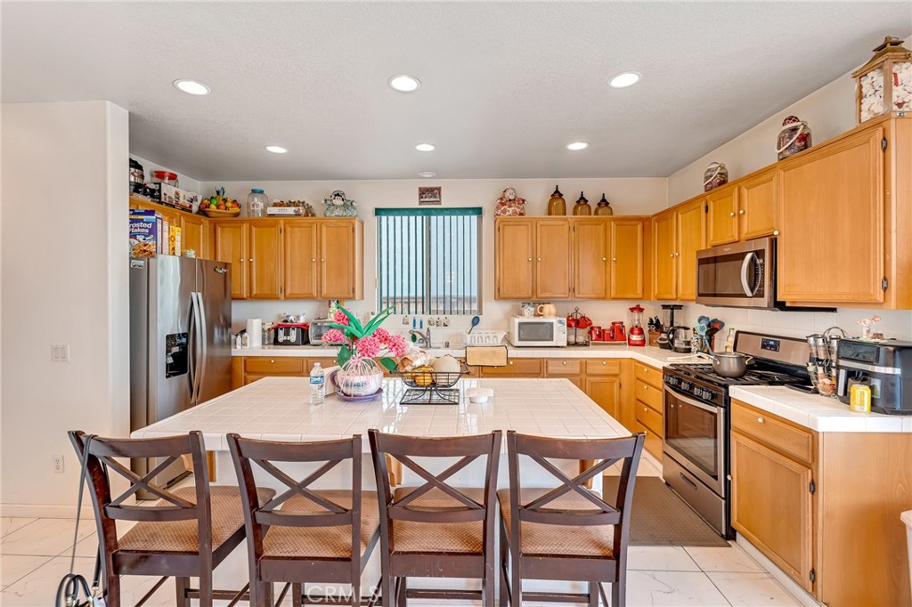 11036 Windcrest Court Adelanto, CA 92301 - Photo 9 of 45 a kitchen with stainless steel appliances granite countertop a table chairs microwave and sink