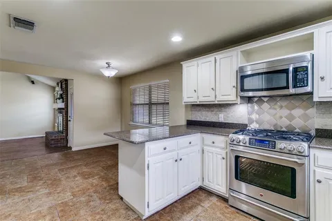 a kitchen with stainless steel appliances granite countertop a stove a sink a microwave a refrigerator and white cabinets