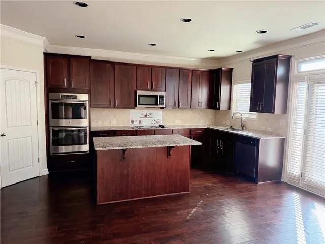 a kitchen with kitchen island granite countertop wooden floors stainless steel appliances and sink
