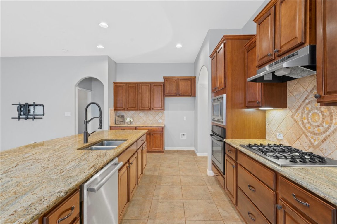 1813 Tall Chief Leander, TX 78641 - Photo 12 of 26 Kitchen with arched walkways, light stone countertops, a sink, under cabinet range hood, and stainless steel appliances