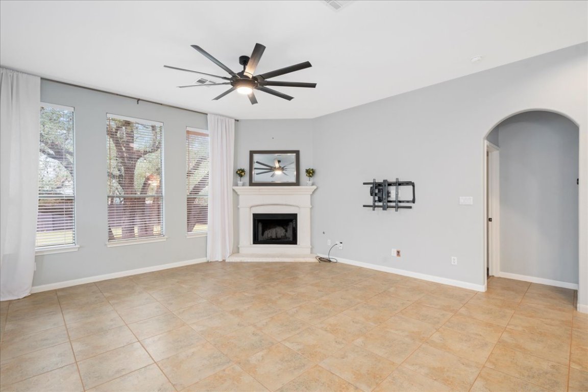1813 Tall Chief Leander, TX 78641 - Photo 13 of 26 Unfurnished living room featuring a fireplace with raised hearth, arched walkways, baseboards, and ceiling fan