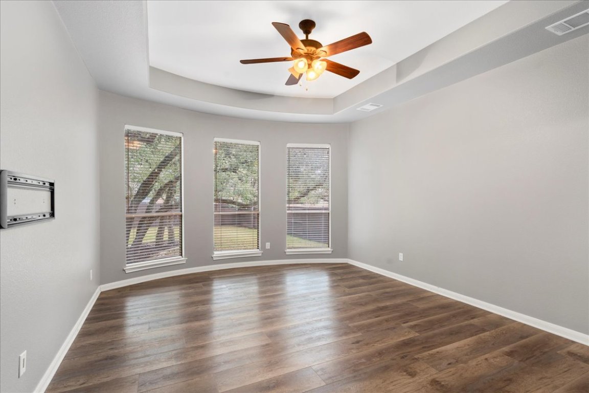1813 Tall Chief Leander, TX 78641 - Photo 15 of 26 Unfurnished room with visible vents, dark wood-style flooring, baseboards, ceiling fan, and a raised ceiling