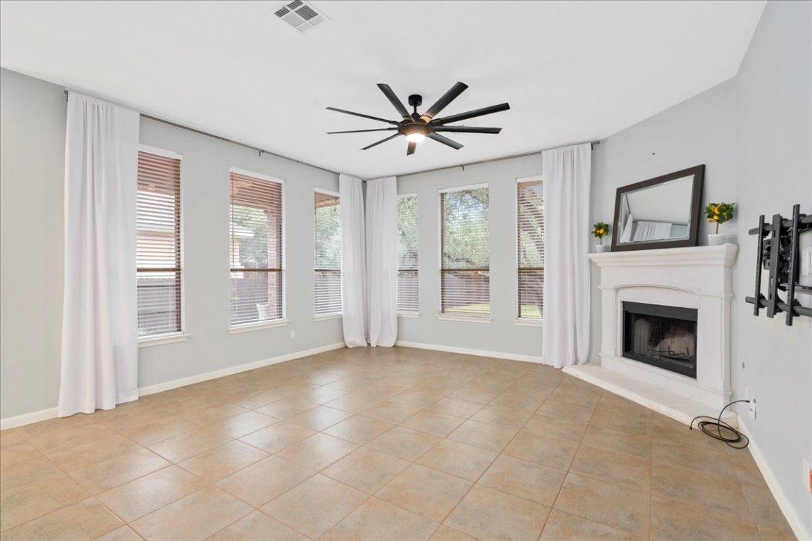 1813 Tall Chief Leander, TX 78641 - Photo 4 of 26 Unfurnished living room featuring light tile patterned flooring, a fireplace with raised hearth, a ceiling fan, baseboards, and visible vents