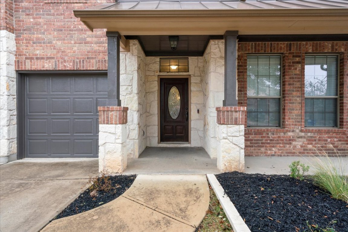 1813 Tall Chief Leander, TX 78641 - Photo 6 of 26 Doorway to property featuring stone siding, a garage, concrete driveway, a standing seam roof, and metal roof