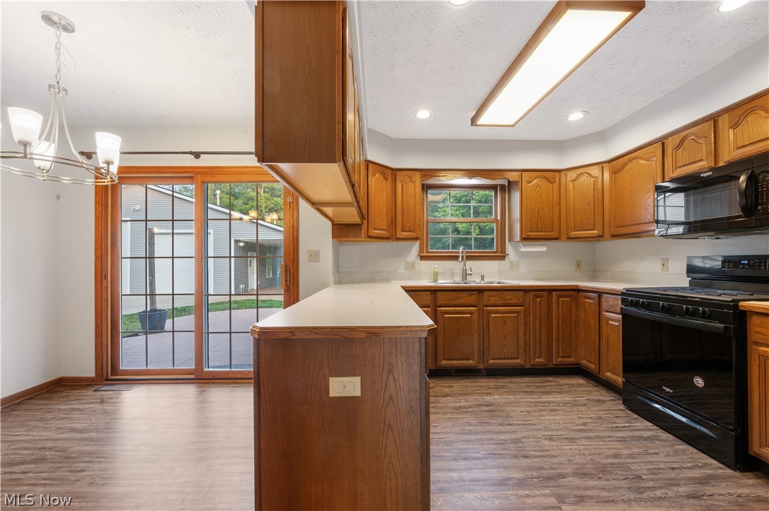 Kitchen featuring black appliances, hardwood / wood-style floors, sink, decorative light fixtures, and a notable chandelier