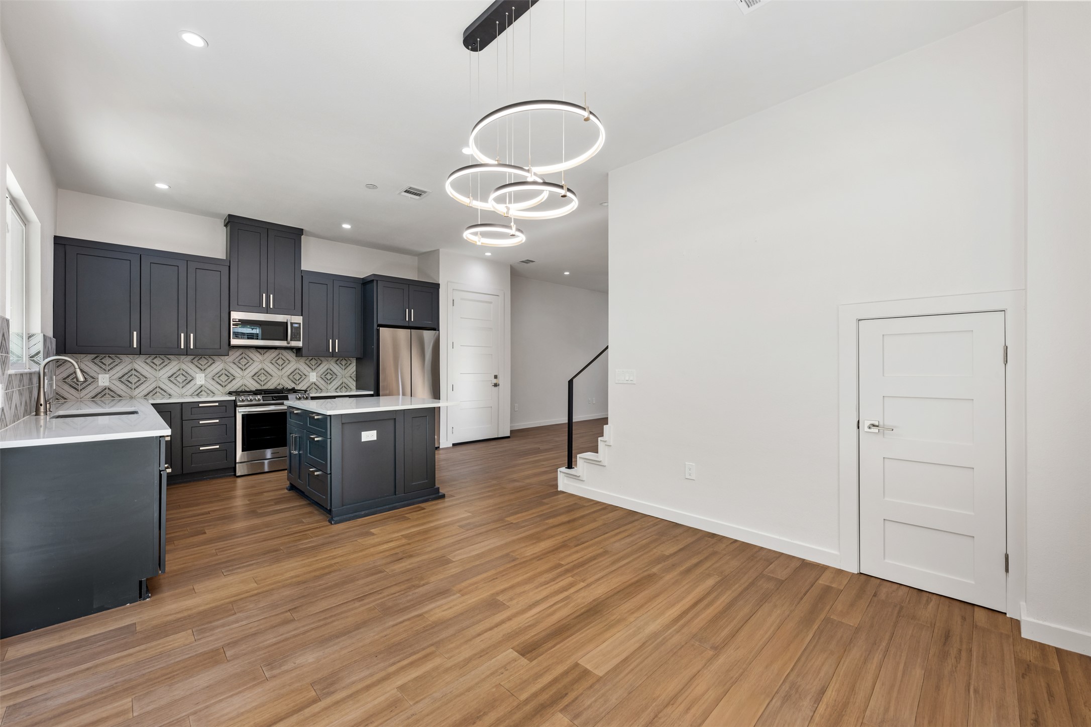 3010 Webberville Road, Unit 1 Austin, TX 78702 - Photo 26 of 38 Open-concept kitchen and living area featuring wood-finish flooring, dark cabinetry, stainless steel appliances, a kitchen island, and contemporary ring-style lighting fixtures