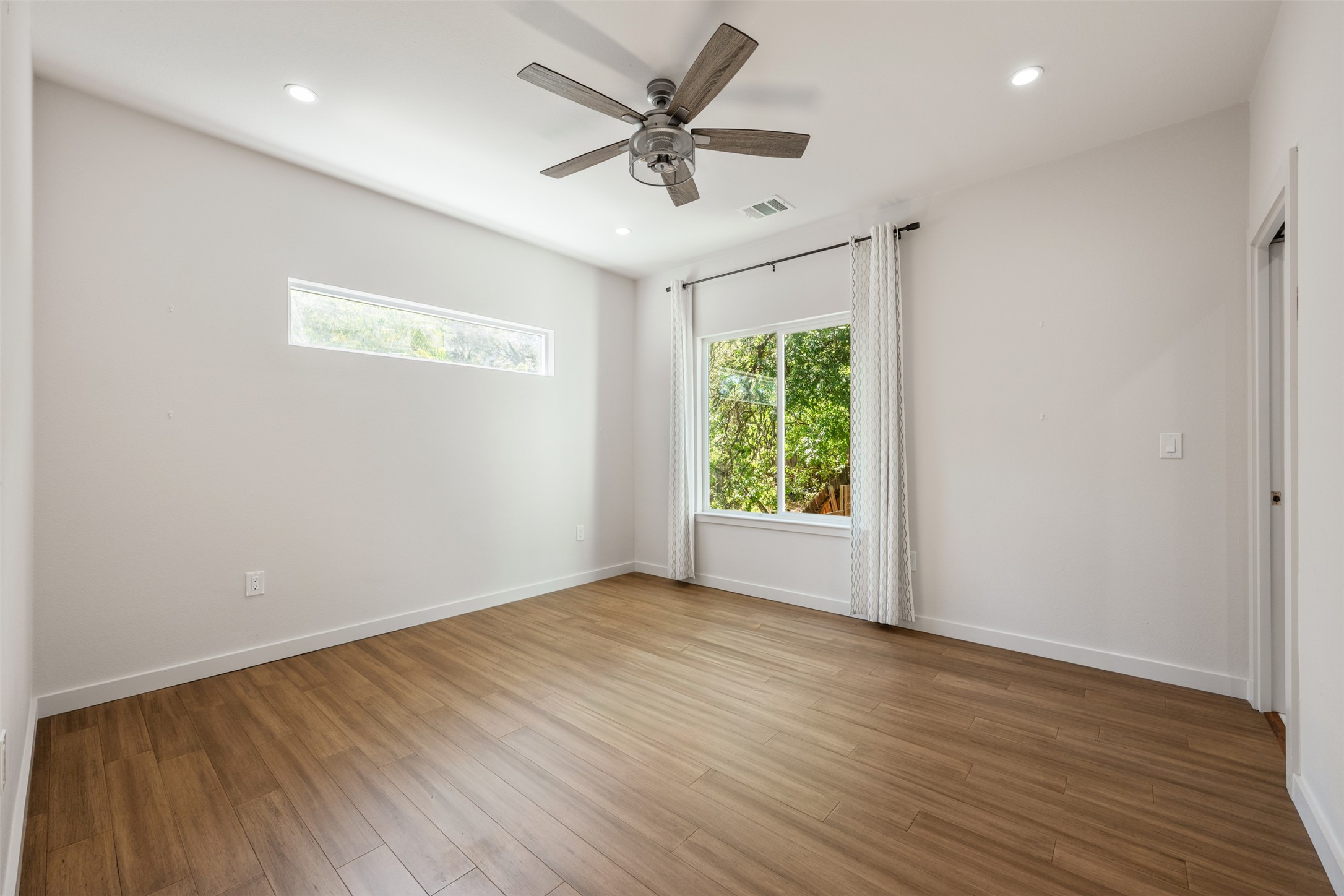 3010 Webberville Road, Unit 1 Austin, TX 78702 - Photo 30 of 38 Spacious room featuring wood-finish flooring, a contemporary ceiling fan, recessed lighting, a wide window with exterior tree scenery, and an additional high horizontal window