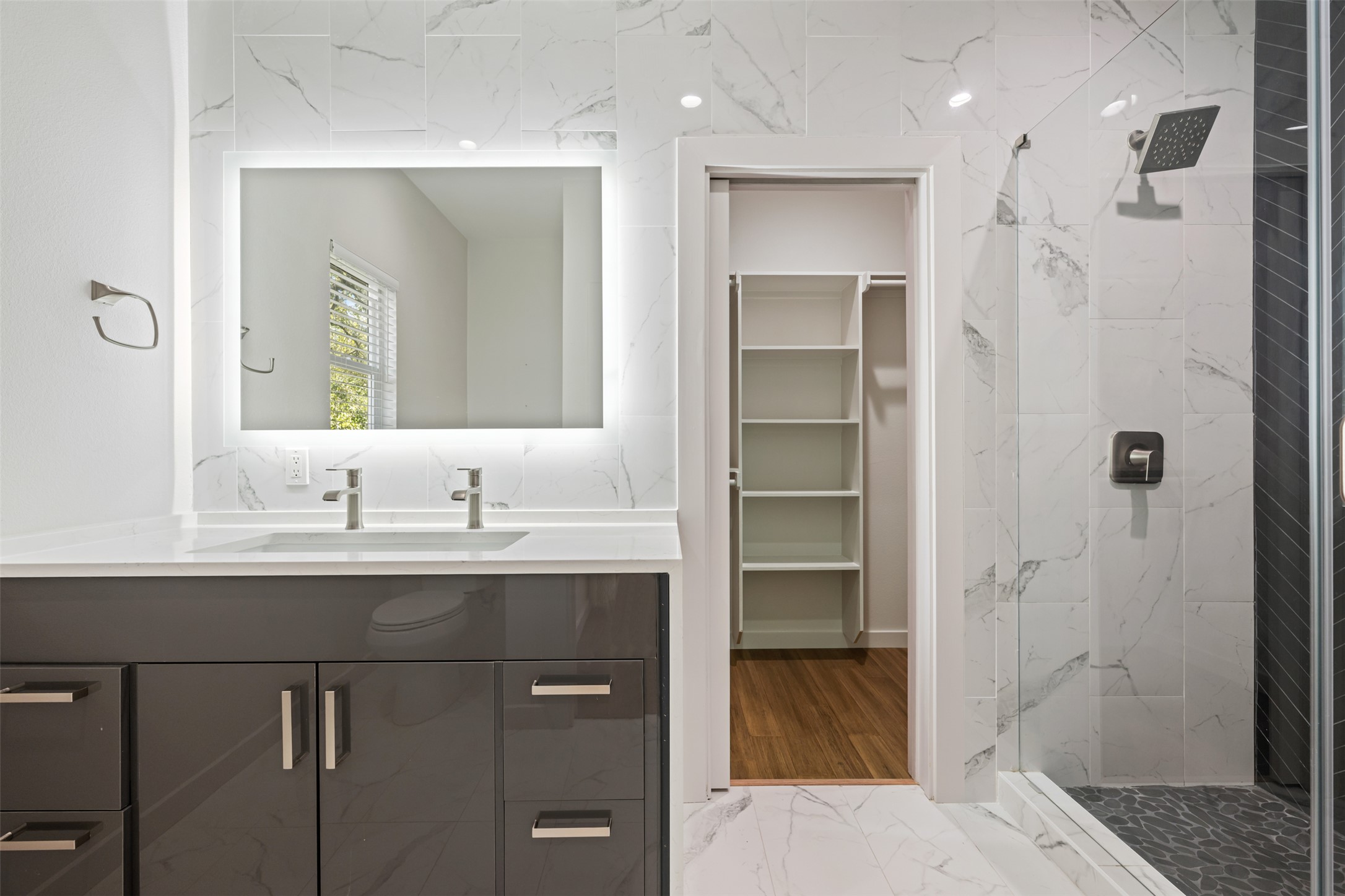 3010 Webberville Road, Unit 1 Austin, TX 78702 - Photo 33 of 38 Bathroom featuring a dual-sink vanity with a white countertop and dark gray cabinetry, an illuminated mirror, and a walk-in shower with a glass enclosure