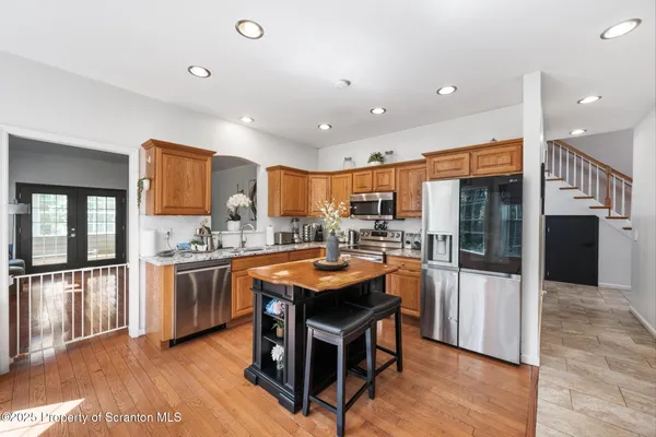 a kitchen with stainless steel appliances granite countertop a refrigerator a sink dishwasher a oven and a dining table with wooden floor